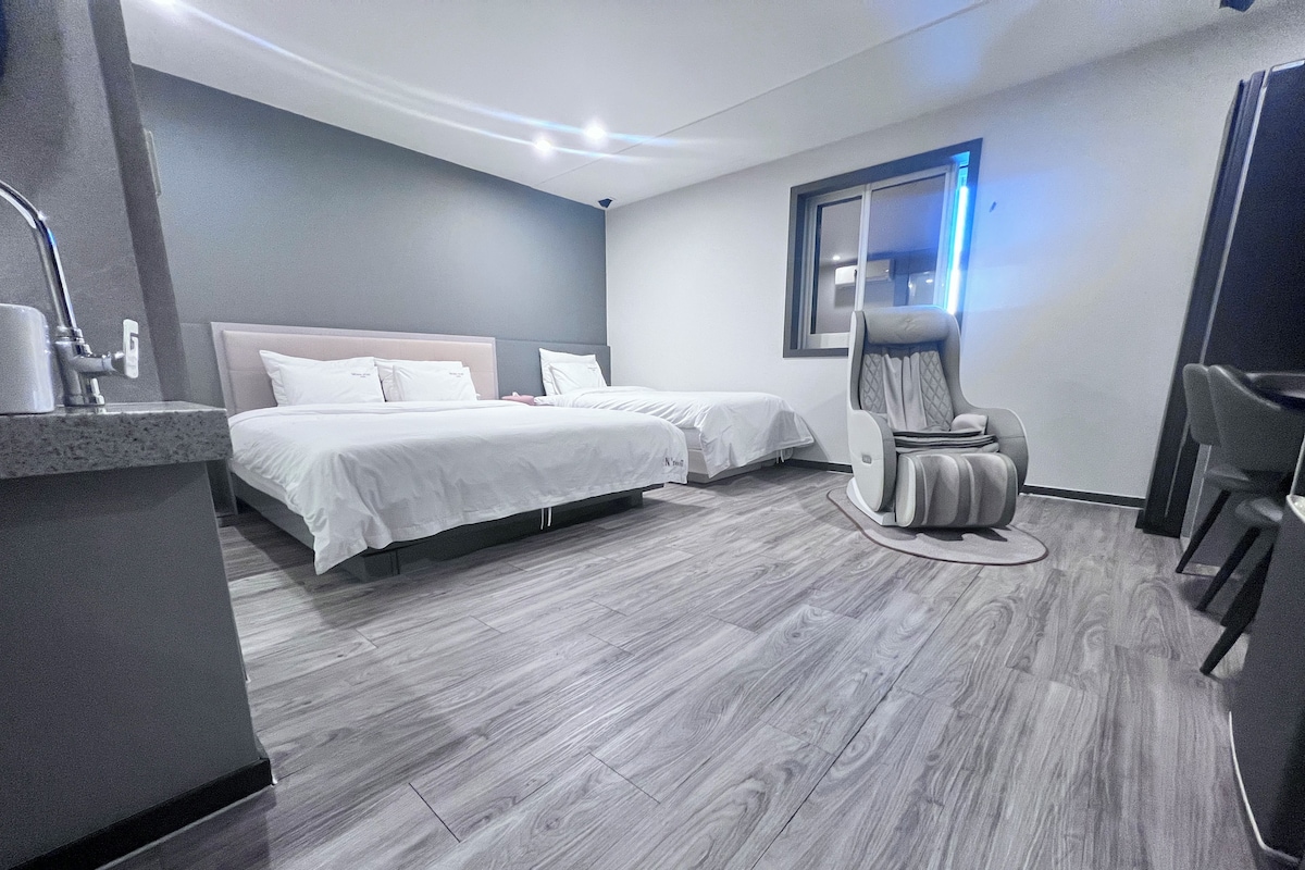 A modern hotel room with a large bed, a massage chair, and a small desk area.
