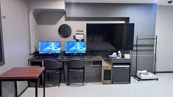 Una habitación moderna con dos monitores, un escritorio, sillas, un televisor de pantalla plana, un refrigerador pequeño y un carrito con objetos.