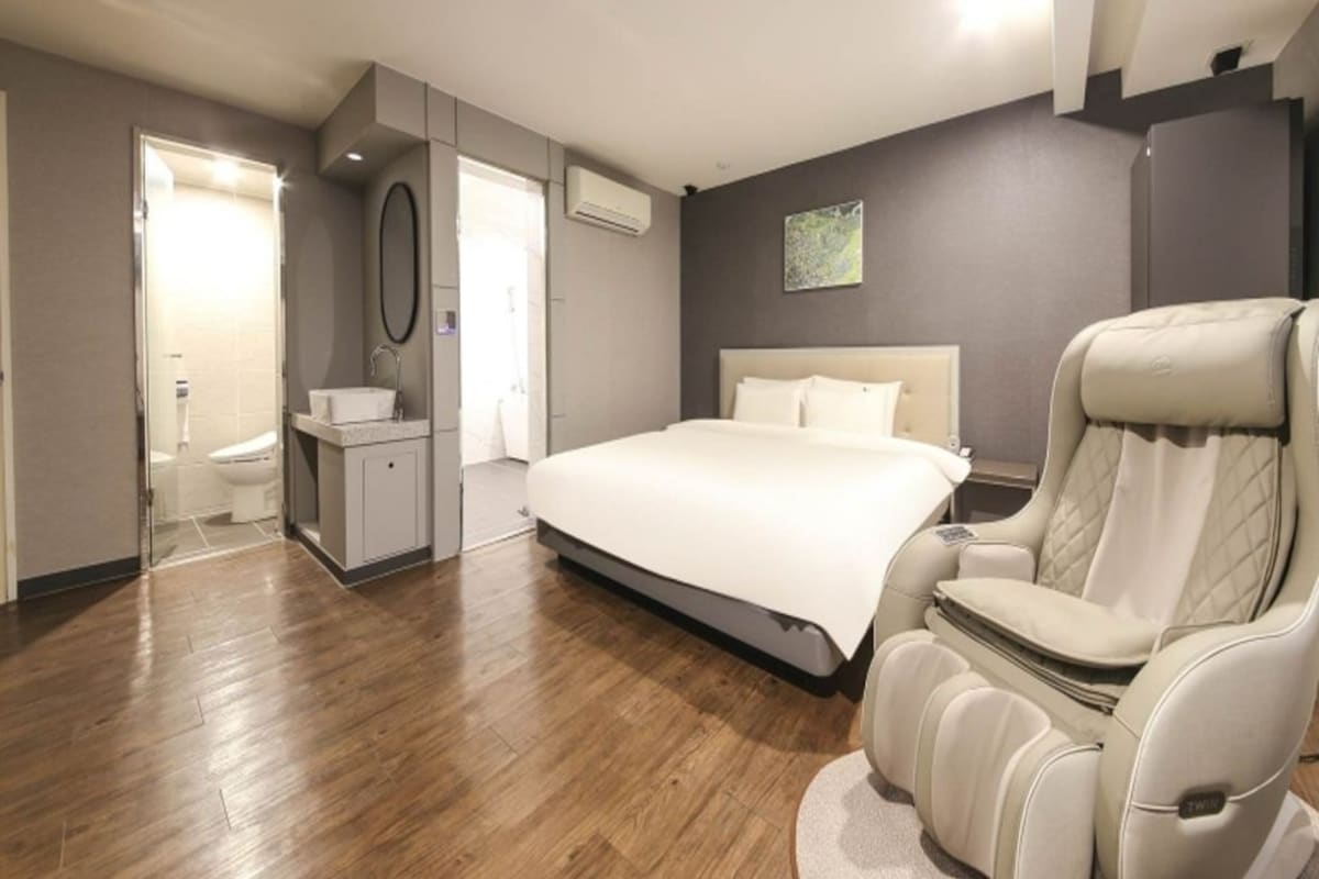 A modern bedroom with a large bed, a massage chair, and a small bedside table.