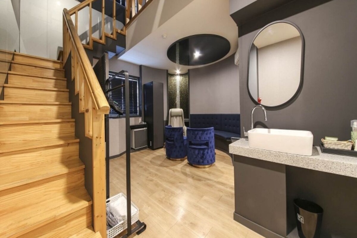 A modern interior with a wooden staircase, a kitchen area, and a bathroom with a round mirror.