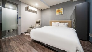 A modern hotel room with a large bed, a chair, a wall-mounted air conditioner, and a painting of sunflowers. - MORASTAY (Busan)