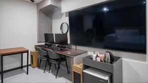 A modern hotel room with a large flat-screen TV, a desk with two monitors, a coffee machine, and a small cabinet. - MORASTAY (Busan)