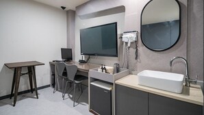 A modern bathroom with a large mirror, a sink, a toilet, a desk with a chair, and a flat-screen TV. - MORASTAY (Busan)