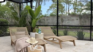 Een terras met twee rieten loungestoelen, een geweven mand, een hoed en een paar slippers.