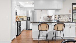 Een moderne keuken met witte kasten, een centraal eiland, twee barkrukken en een inbouwoven.