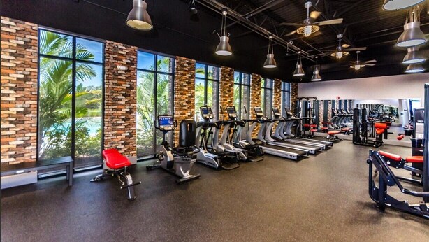 Ett gym med träningsutrustning, stora fönster och en tegelvägg.