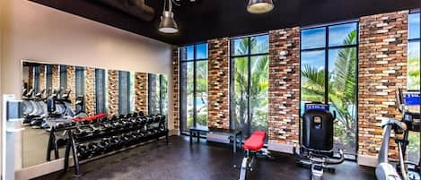 A gym with exercise equipment, large windows, and a brick wall.
