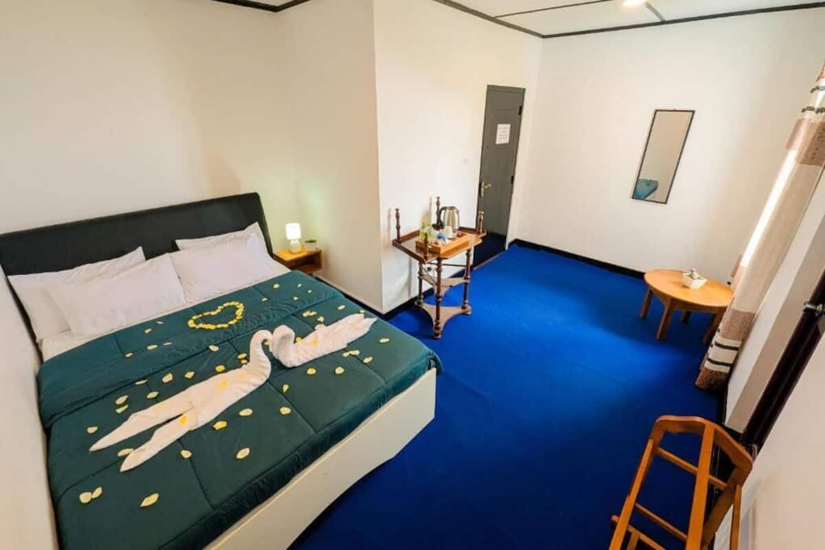 A hotel room with a bed, a small table with a lamp, a chair, and a desk with a chair.