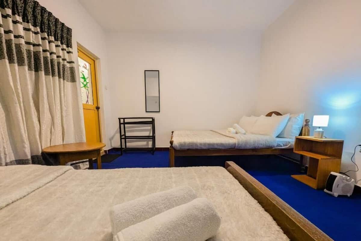 A hotel room with two beds, a wooden nightstand, a lamp, and a small table.