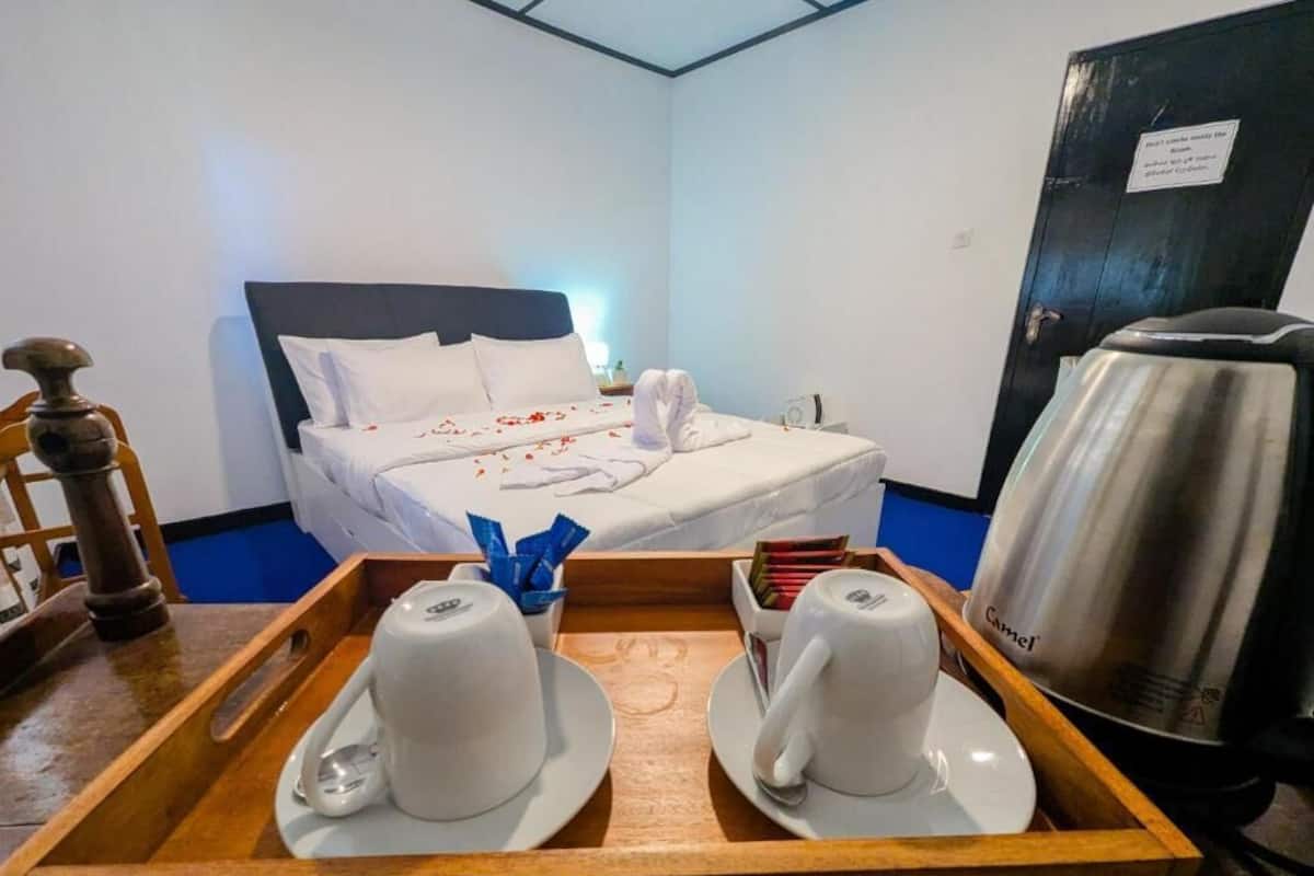 A hotel room with a neatly made bed, a tray with two cups and saucers, a kettle, and a cabinet.