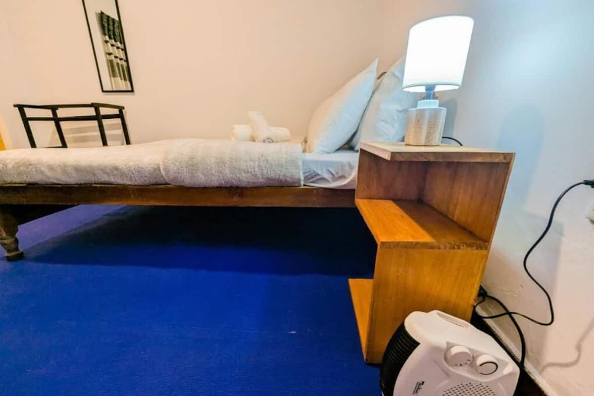 A bedroom with a bed, a bedside table with a lamp, a wooden nightstand, and a white portable heater.