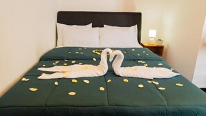 A bed with a dark green bedspread, white pillows, and a headboard. There are two white towels arranged in a swan shape on the bed. - The Crown's Lodge Misty Hideaway  (Nuwara eliya)