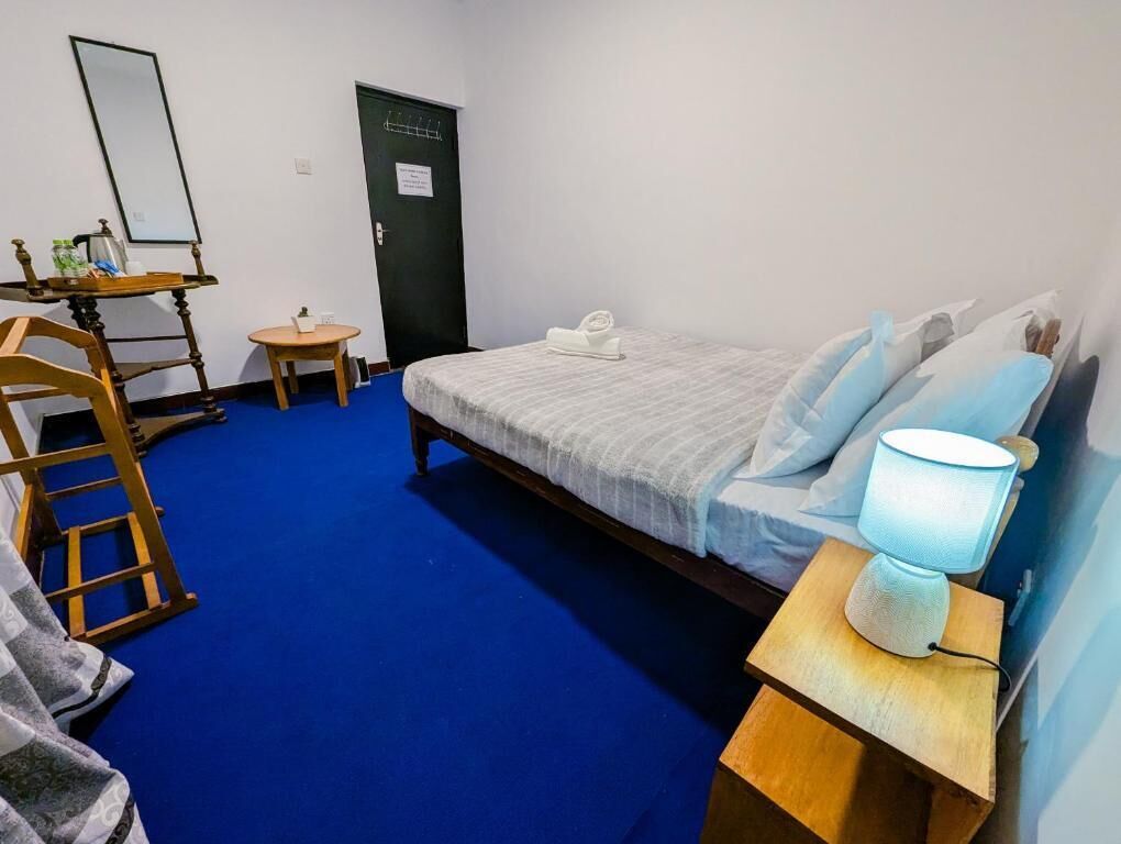 Quarto com cama, escrivaninha com cadeira, mesinha, abajur e porta.