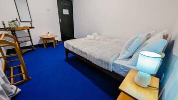 Quarto com cama, escrivaninha com cadeira, mesinha, abajur e porta.