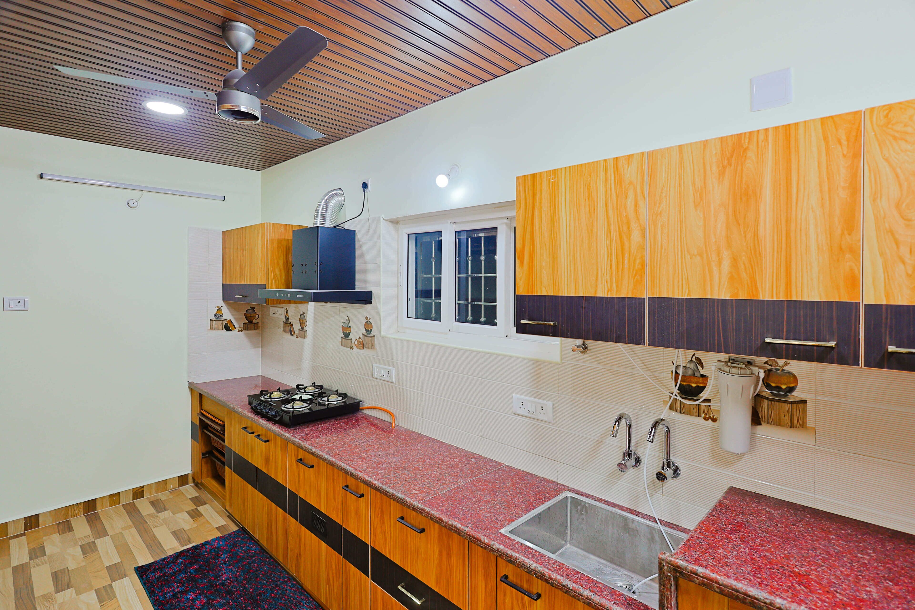 A kitchen with wooden cabinets, a red countertop, a window, and a ceiling fan.