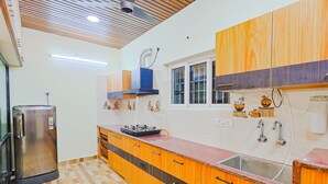 A kitchen with wooden cabinets, a stainless steel refrigerator, a gas stove, and a window with a view. - Cozy Apartment w/Living room,WIFI,Kitchen,Laundry & Parking in Velachery,Chennai (Chennai)