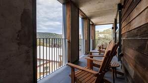 A balcony with wooden chairs, large windows, and a view of a hilly landscape. - Nelse Lodge (Falls Creek)