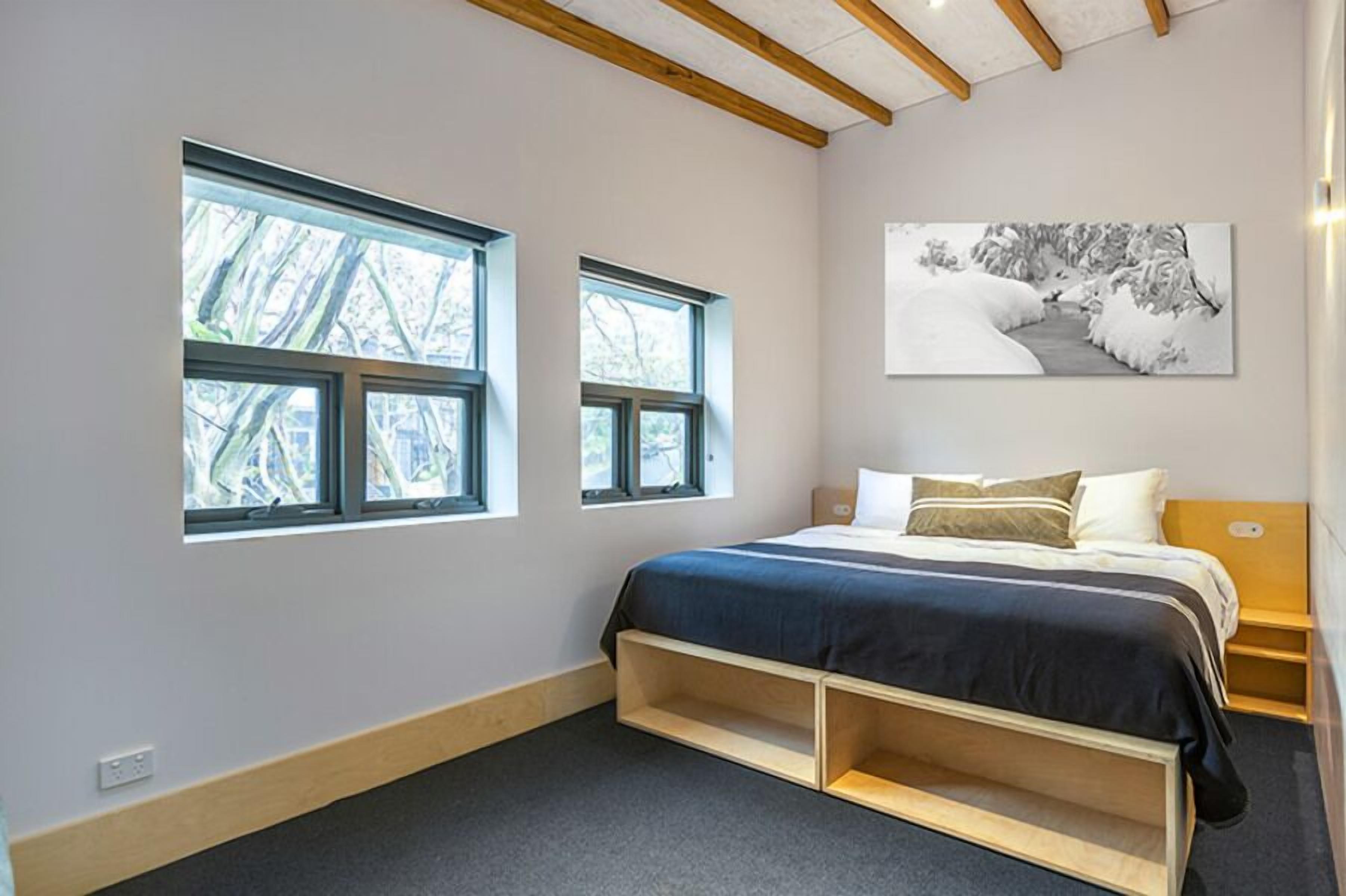 Een slaapkamer met een bed, twee ramen, een schilderij en inbouwkasten.