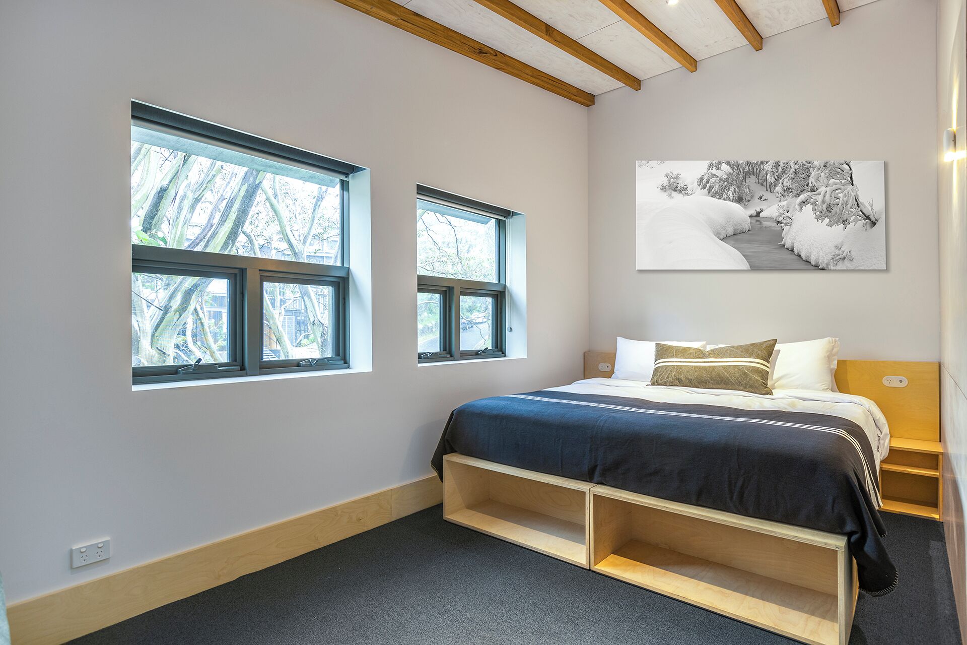 A bedroom with a bed, two windows, a painting, and a wooden headboard.
