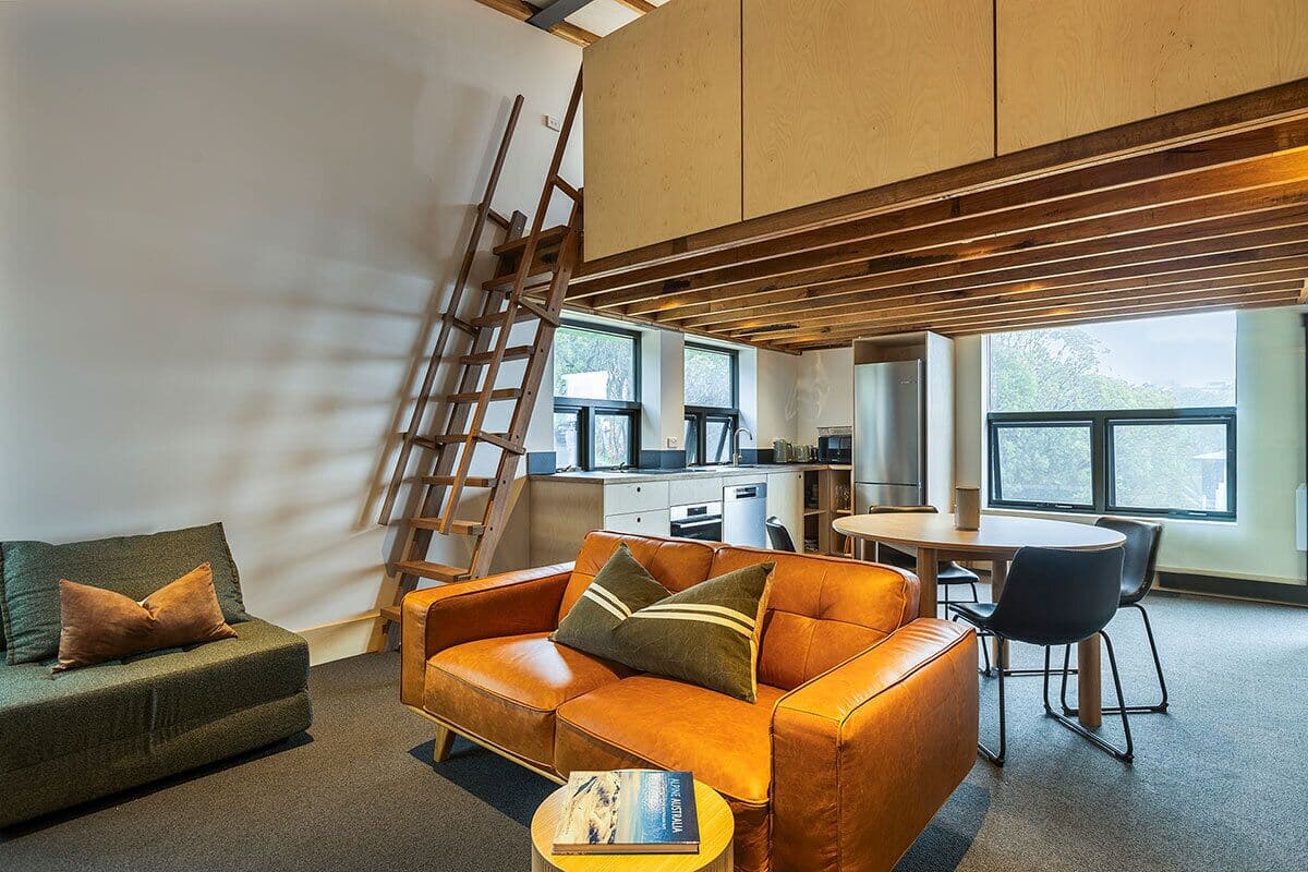 Un salon moderne avec un canapé, une table basse et un coin repas avec des chaises. Une échelle est appuyée contre le mur.