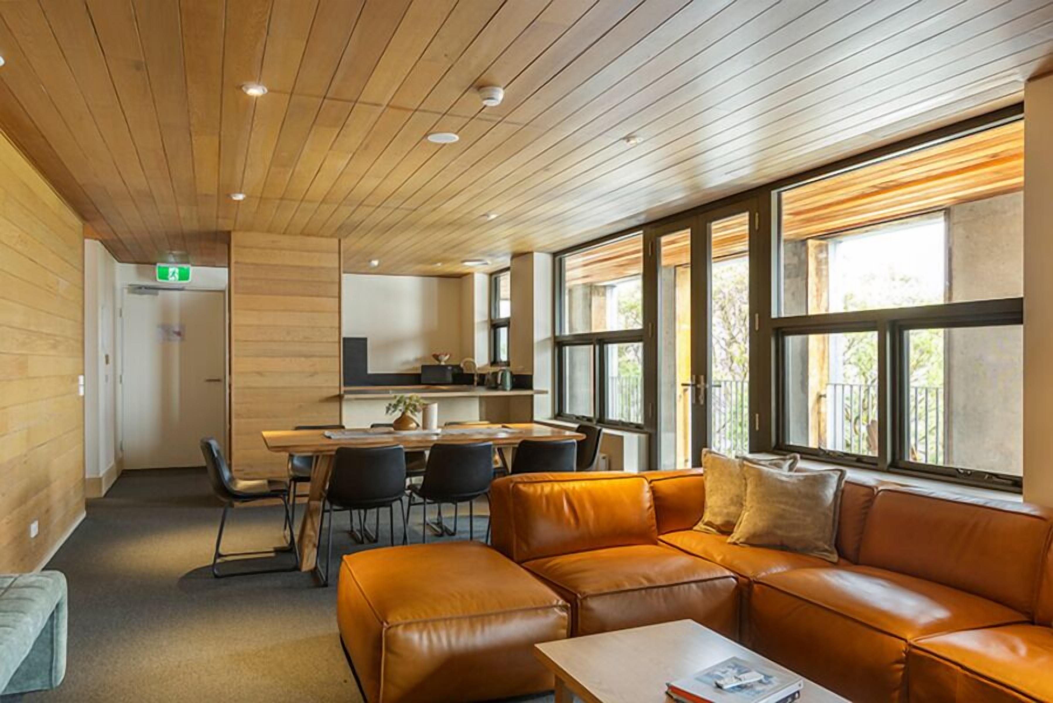 Un intérieur moderne avec un plafond en bois, un canapé en cuir, un coin repas et de grandes fenêtres.