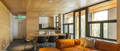Un intérieur moderne avec un plafond en bois, un canapé en cuir, un coin repas et de grandes fenêtres.
