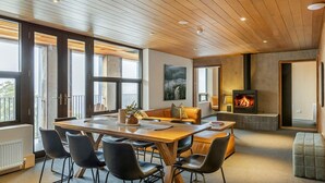 A modern living room with a wooden ceiling, a fireplace, a dining table with chairs, and a sofa. - Nelse Lodge (Falls Creek)