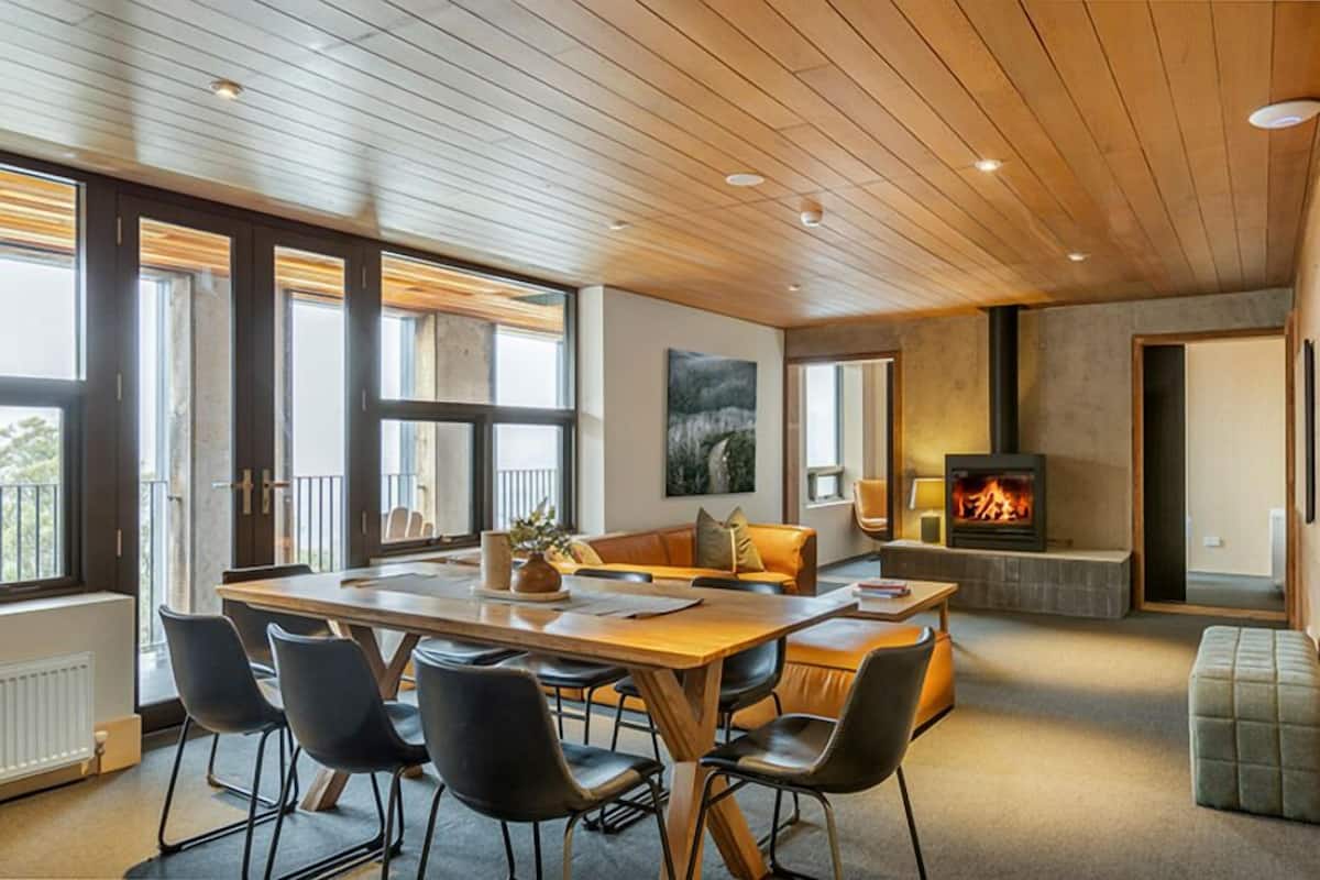 Un salon moderne avec un plafond en bois, une cheminée, une table à manger avec des chaises et un canapé.