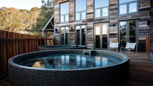 A modern house with a wooden exterior, a large deck, and a hot tub. - Nelse Lodge (Falls Creek)