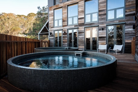 A modern house with a wooden exterior, a large deck, and a hot tub.
