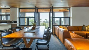 A modern dining area with a wooden table, black chairs, and a leather couch. - Nelse Lodge (Falls Creek)
