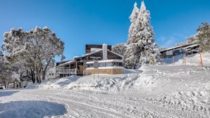 A modern building with a ski lift, surrounded by snow-covered trees and a clear blue sky. - Nelse Lodge (Falls Creek)