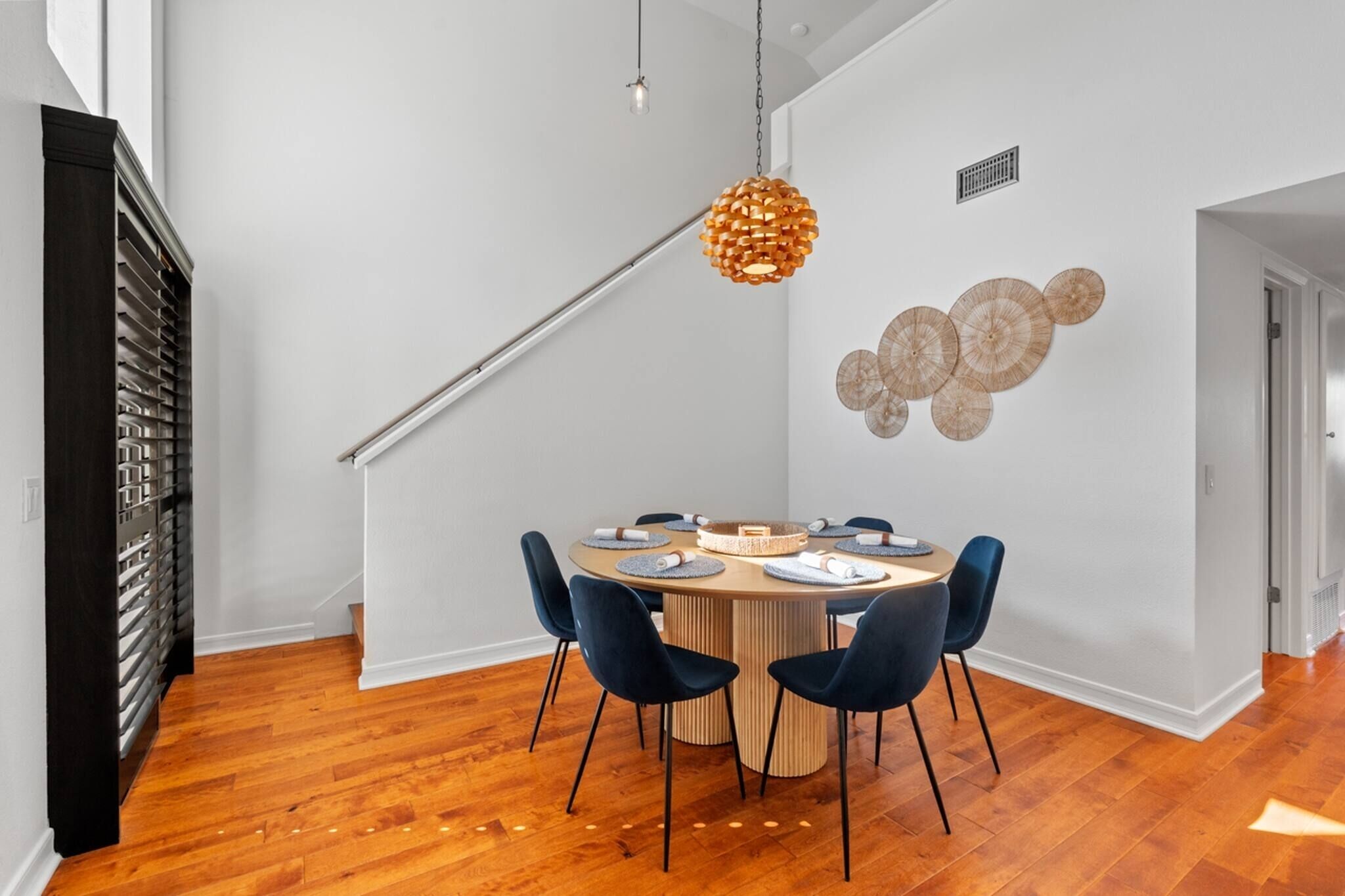 A dining area with a round table, chairs, and a hanging light fixture.