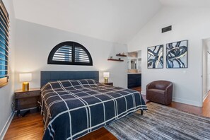 A bedroom with a bed, bedside tables, a chair, a window with blinds, a rug, and artwork on the wall. - Turf & Tide: Rare Triple Crown Home – Near Beach (Solana Beach)