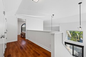 A hallway with wooden flooring, white walls, and a view of a room with a bed. - Turf & Tide: Rare Triple Crown Home – Near Beach (Solana Beach)