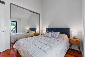 Une chambre à coucher avec un grand lit, deux tables de chevet, une commode, un miroir et une porte donnant sur un balcon.