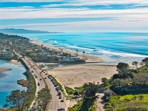 A coastal road with a beach and ocean on the right, a bridge on the left, and a hilly landscape in the background. - Turf & Tide: Rare Triple Crown Home – Near Beach (Solana Beach)