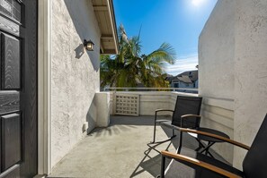 Ein Balkon mit Betonboden, einem schwarzen Stuhl, einem kleinen Tisch und einer Wandleuchte.