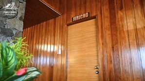 Une porte en bois sur laquelle est inscrit le nom « JERICHO », située dans une pièce aux murs lambrés et ornée d’un mur en pierres apparentes.