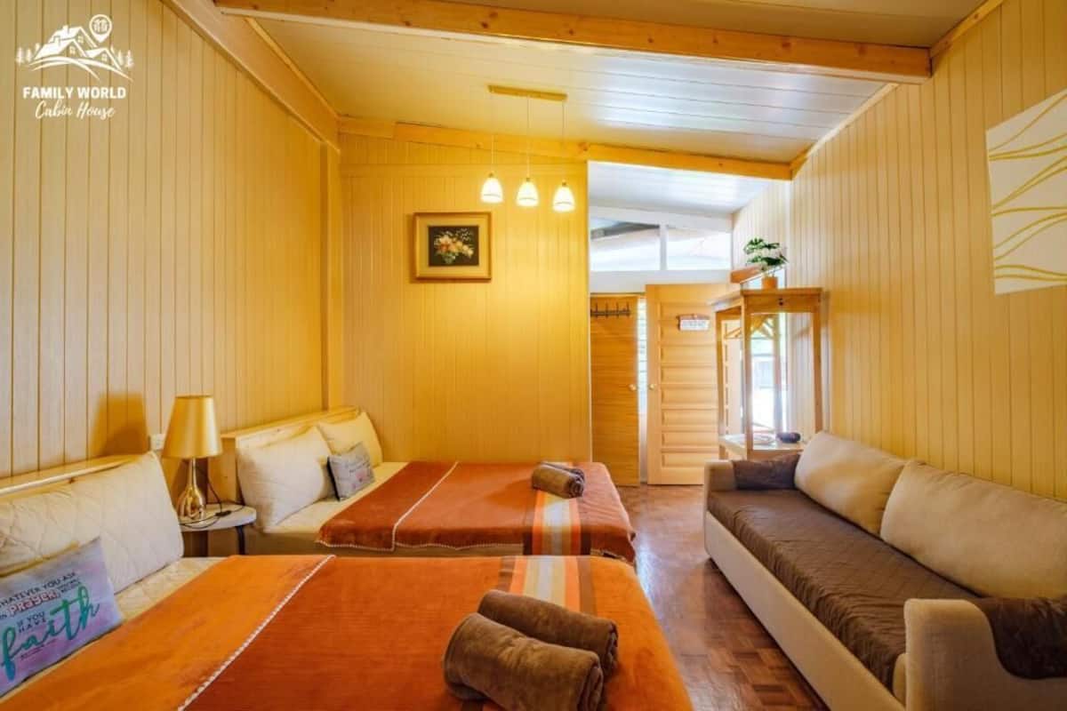 Een kamer in chaletstijl met houten wanden, een bed met oranje dekbed, een bank, een kleine tafel met een lamp, en een foto aan de muur.