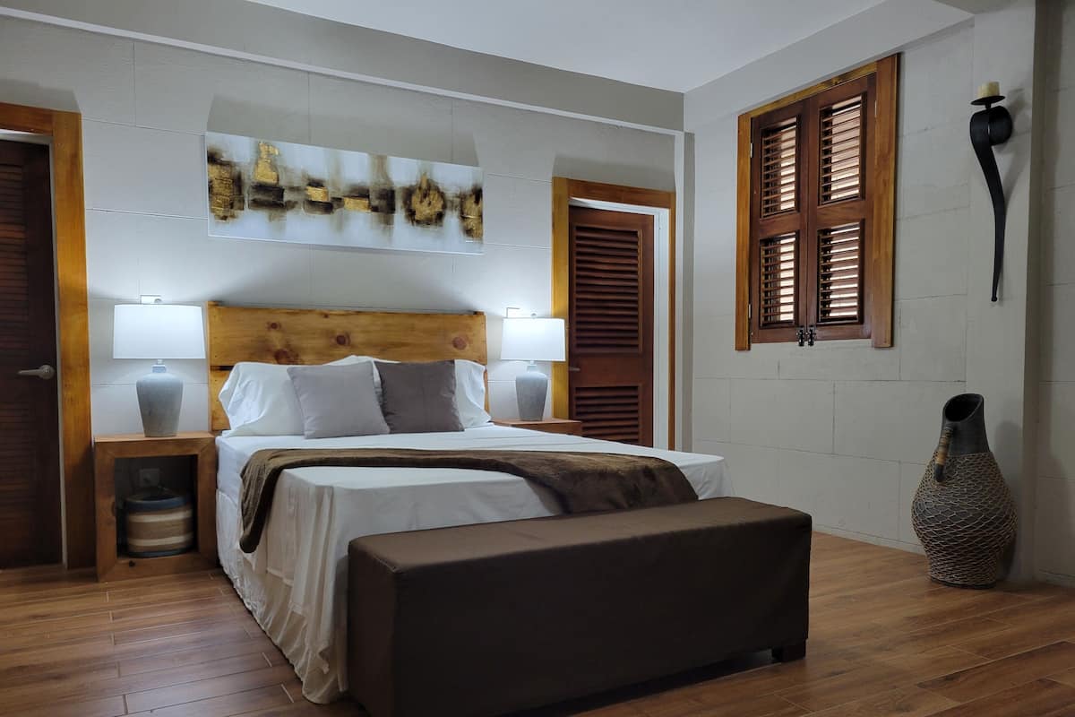 A bedroom with a bed, bedside tables, a bench, a wall-mounted lamp, and a decorative vase.