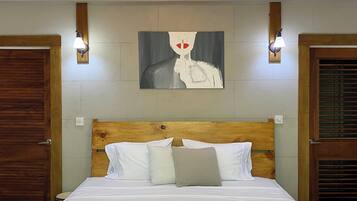 A hotel room with a wooden headboard, a bed with white bedding, a painting on the wall, and two wall-mounted lamps.