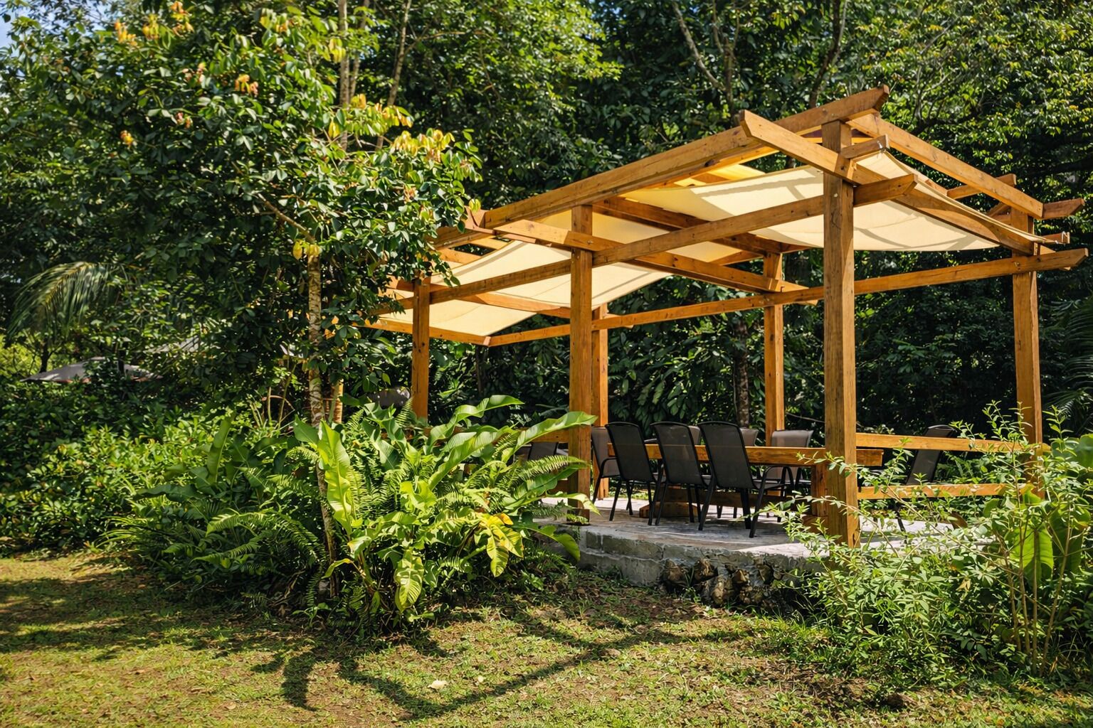 En pergola i træ med et bord og stole under, omgivet af frodigt grønt.