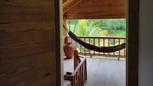 A wooden deck with a hammock and a table, overlooking a lush garden. - Sabifi River Resort (Castle Bruce)