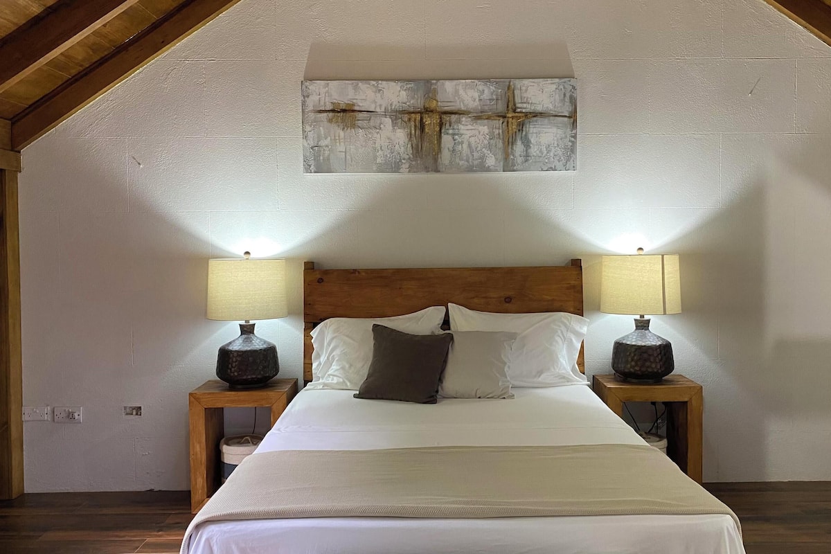 A bedroom with a wooden headboard, two bedside lamps, a bed with white bedding, and a painting on the wall.