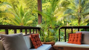 A wooden deck with a sofa and a bench, surrounded by lush greenery and a wooden railing. - Sabifi River Resort (Castle Bruce)