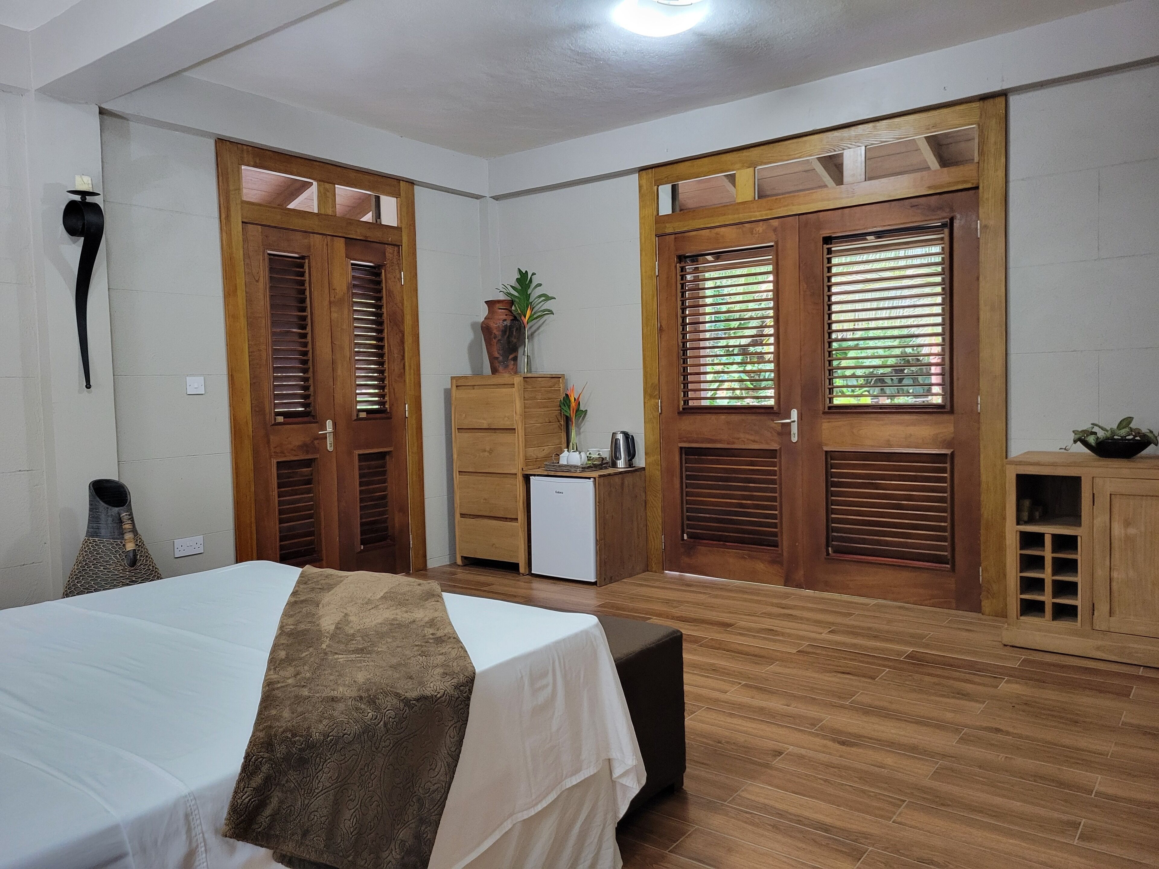 Une pièce comprenant un lit, un petit bureau, une armoire et deux portes avec des volets.