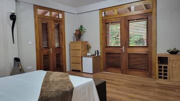 Une pièce comprenant un lit, un petit bureau, une armoire et deux portes avec des volets.