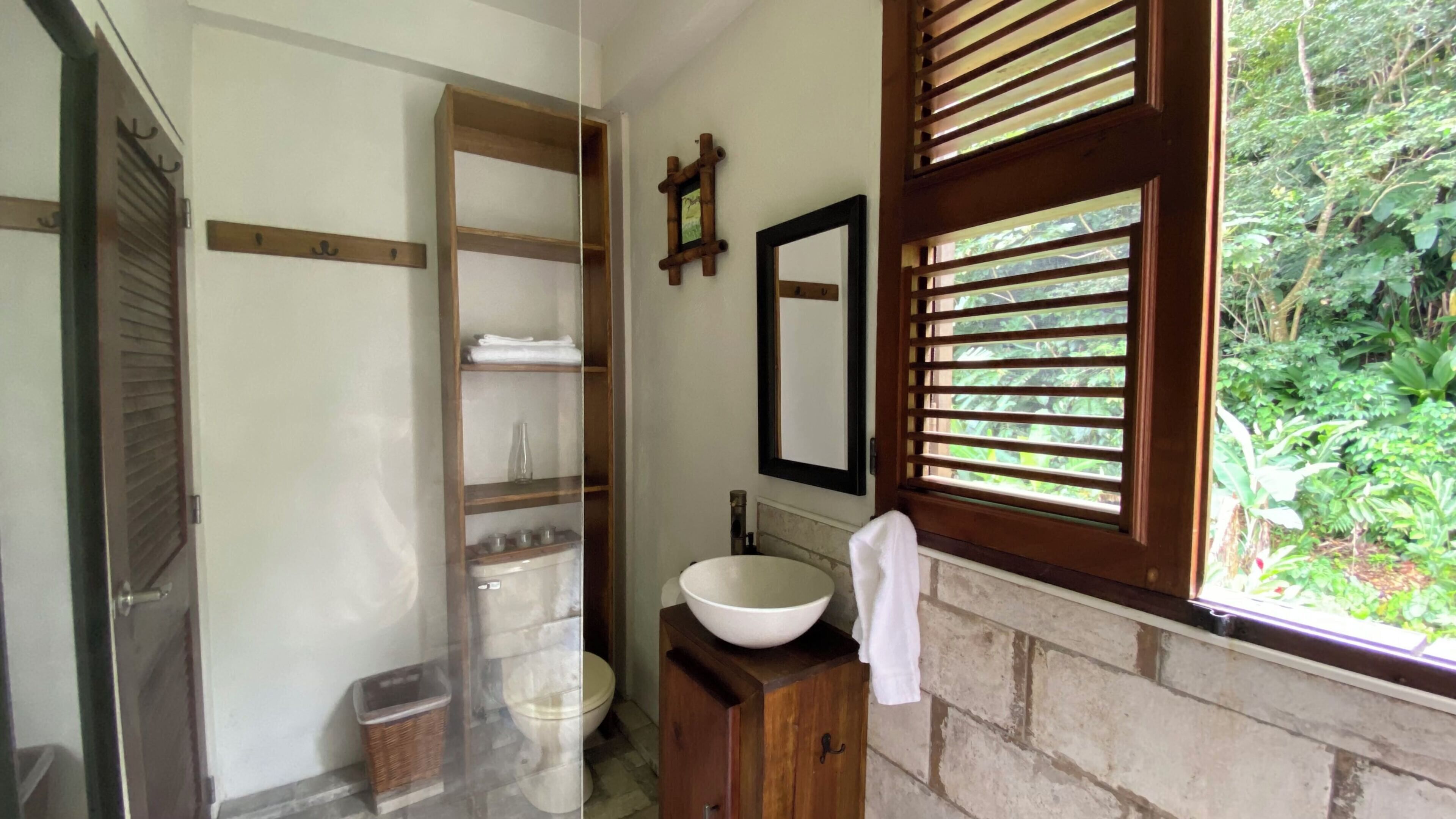 A bathroom with a wooden vanity, a large white basin, a mirror, and a window with shutters.