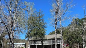 A wooden dock extending over a calm body of water, with a building featuring a covered area and outdoor seating in the background. - Beautiful views on Lake Wateree with large screened in porch, 3 bedroom, 2 bath. (Camden)
